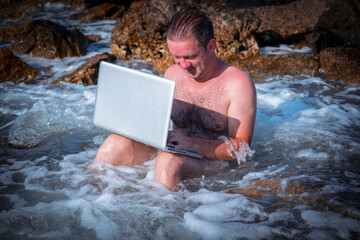 Humorous image of businessman working with a laptop on the stones beach of sea.