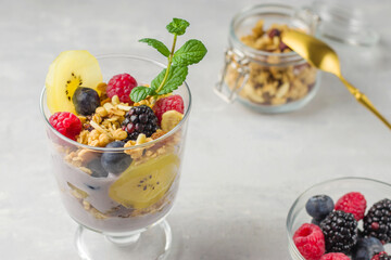 Vegan natural dessert. Granola with raspberries, blueberries, golden kiwi and mint sprig. A glass of muesli, berries and a yoghurt parfait on the table. Selective focus.