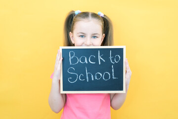 schoolgirl holding a tablet in her hands with the inscription Back to school on a yellow