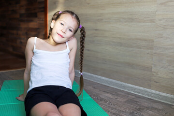 girl child in sportswear on a rubber gymnastic mat shows a healthy lifestyle, always having fun and in good shape