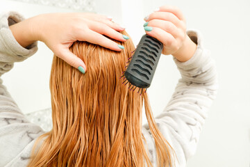 Fototapeta premium A blonde woman tries to comb her tangled hair with a comb after bathing. Blond red combing wet and tangled hair.