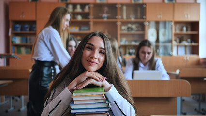 A student poses with textbooks at her desk in her class.