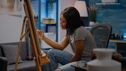 Black young adult with creative imagination drawing while sitting in workshop room. African american artist looking at white vase and creating beautiful masterpiece for modern art project