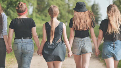 Schoolgirl friends are walking outside the city along a forest road.