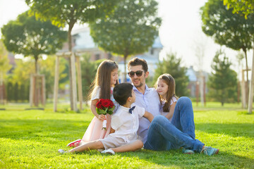 A father and his three children, a boy and two girls, sit on the grass.