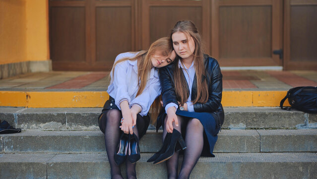 Tired schoolgirls sit barefoot on the steps of the school.
