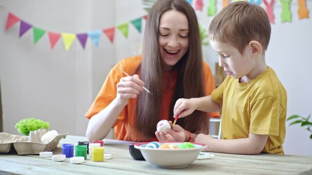 Mom and a child are painting eggs together in a room decorated for the holiday. Concept of preparing the family for Easter, spring mood