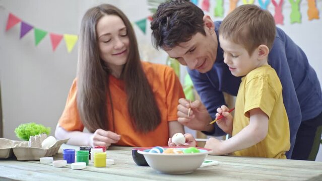 Happy family is coloring Easter eggs in a decorated room and having fun. Mom, dad and child prepare for the holiday