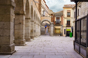 Street and square with stone arches and old houses in the city of Avila, Spain.