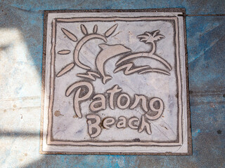 Square iron plate on asphalt with inscription Patong beach. Street art architecture. City art Gray heavy metal hatch on asia road. Manhole cover with text on road. Thailand. Wallpaper and backdrop.