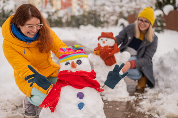 Fototapeta na wymiar Two Caucasian women are making a snowman. Winter fun.