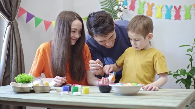 Happy family is coloring eggs in a decorated room and having fun. Mom, dad and child prepare for Easter