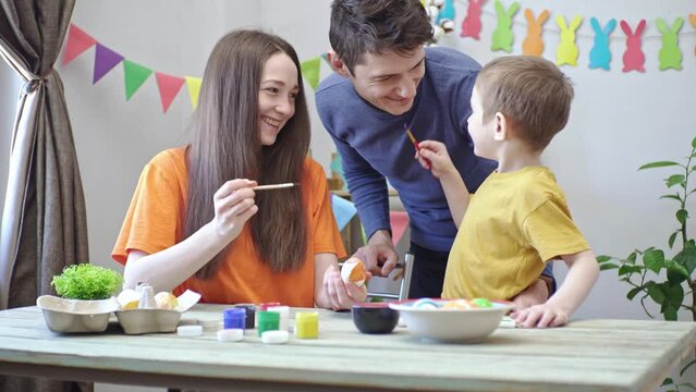 Happy family is coloring Easter eggs in a decorated room and having fun. Mom, dad and child prepare for the holiday