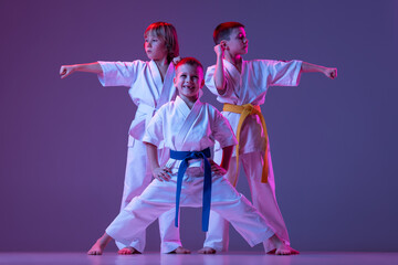 Three sportive kids, little boys, taekwondo or karate athletes in doboks posing isolated on very peri color background in neon. Concept of sport, martial arts © master1305