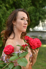 Fototapeta na wymiar beautiful brunette woman with red roses near the bush in the park