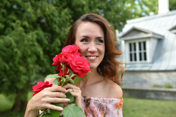 Fototapeta na wymiar beautiful brunette woman with red roses near the bush in the park