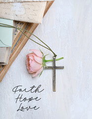 Christian cross, rose flower, old books on white abstract table background. "Faith. hope. love" - religion quote. cross, symbol of Easter, Lent, Christianity religion. flat lay