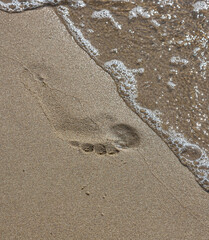 Footprints of a man on the yellow beach sand from walking barefoot by the sea with water that washes away the footprints.