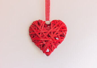 a red wicker heart hangs on a ribbon on a light background. the concept of love, valentine's day and romance. - Powered by Adobe