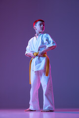 Serious kid, little boy, taekwondo or karate athletes in doboks posing isolated on very peri color background in neon. Concept of sport, martial arts
