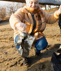 Fototapeta premium Female volunteer picking up a plastic bag from the sandy beach