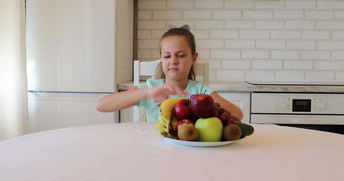 Unhappy child sitting at breakfast. the child does not want to eat vegetables and fruits