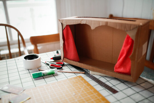 A child plays a homemade cardboard theater at home in a real interior, creative development of children, a happy childhood.