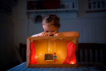 A child plays a homemade cardboard theater at home in a real interior, creative development of...