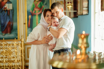 man and woman with baby son in light-colored robes by window in church. 