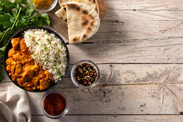 Indian butter chicken in black bowl on wooden table. Top view. Copy space