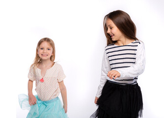 Playful kids, funtime concept. Portrait of cute two girls 6-8 years old wearing light clothes and dancing isolated on white background. Mother's Day, love family, parenthood childhood concept