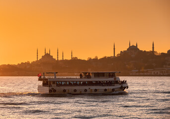 Passenger ferry boat crosses  Bosporus or Strait of Istanbul at sunset. Sultan Ahmed Mosque and the...