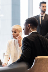 Fototapeta premium blurred businesswoman talking on smartphone near interracial bodyguards in hotel lobby.
