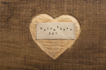 Valentine's day - tiny typed text note close up. Valentines Day greetings concept. Carved heart shape on wood as background for Valentines greeting card.