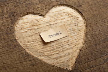 Love to travel concept. Travel - tiny typed text note close up, carved heart shape on wood as a background.