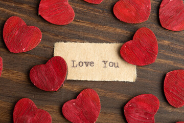 Love you - typed text. Valentines Day greetings concept. Little red wooden hearts close up....