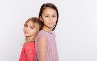Two stylish friends or sisters kid girls stand with their backs to each other. Girls wearing pink dress and standing back to back isolated over white background
