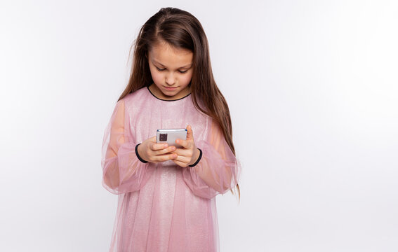 Caucasian kid girl look at screen of mobile phone watching video or typing text, isolated over white background free space for you text
