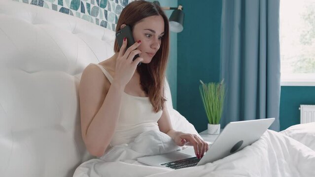 pretty girl in pajamas in bed talking on the phone and working on a laptop