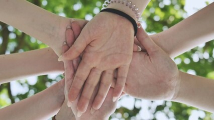 Girlfriends girls join hands in the summer against the background of tree branches.
