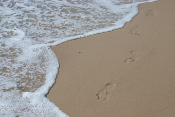 Footprints in the sand beach. Footprints in the sand against a sea wave. Footprints on a sunny day with golden sand, beach, wave and footsteps