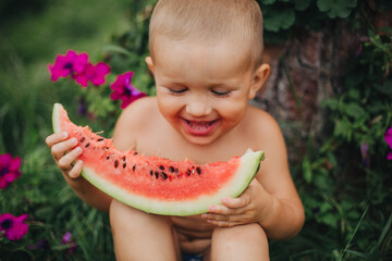 Little boy eating watermelon on green grass. Childhood in the village. Happy child eating watermelon.