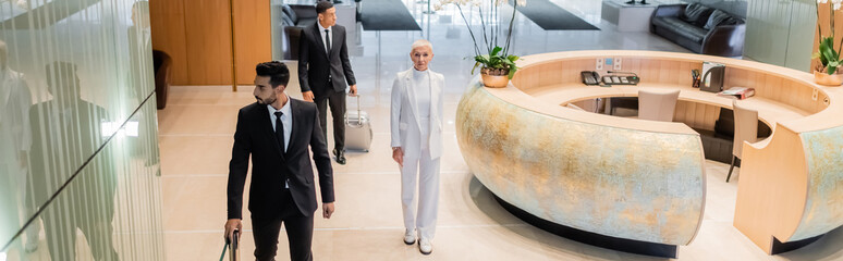 high angle view of stylish senior businesswoman near multiethnic private bodyguards in hotel lobby,...