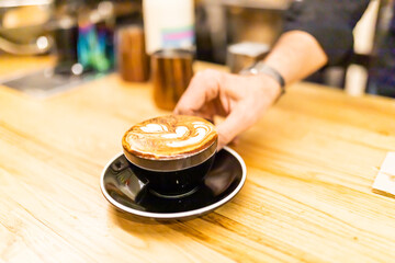 Fototapeta na wymiar unrecognizable barista offering latte with latte art on a coffee shop bar