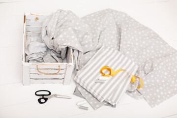 process of sewing of bed linen. Sewing kit. Grey fabric, scissors, threads, measuring tape and white old wooden box on white wooden background