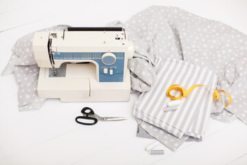 process of sewing of bed linen on sewing machine. Sewing kit. Grey fabric, scissors, threads, measuring tape and sewing machine on white wooden background