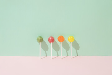 Colorful lollipops leaning against a green wall and a pink background. Minimal candy lay out concept