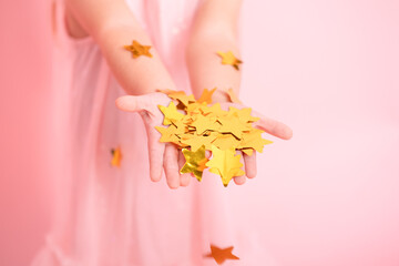 close up of child hands with gold confetti. kid in pink dress celebrating birthday