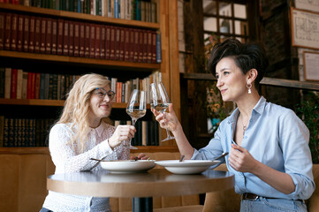 Two middle-aged women cheering with wine at restaurant.