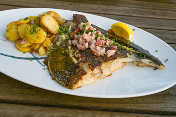 Fried plaice with bacon and potatoes on a plate and a rustic wooden table, selected focus
